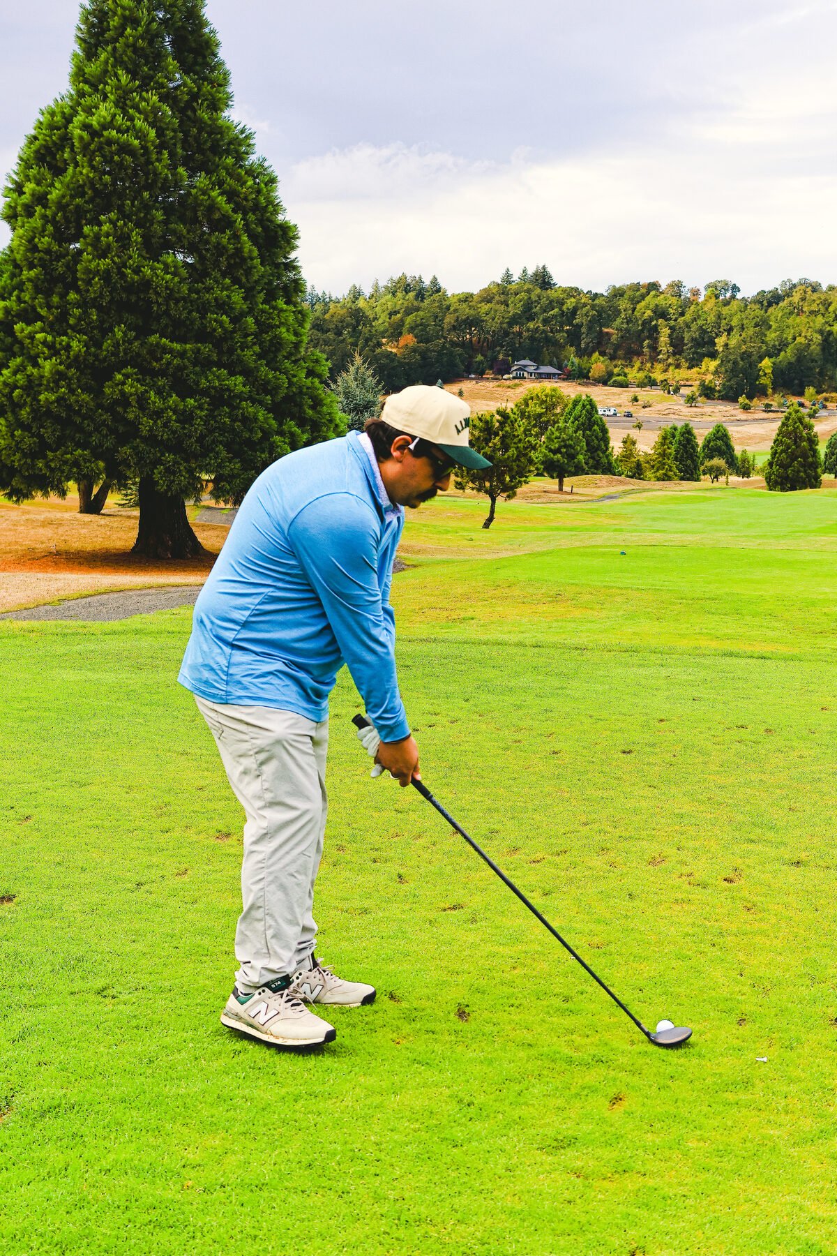Addressing the ball in a blue quarter zip, tee box wide