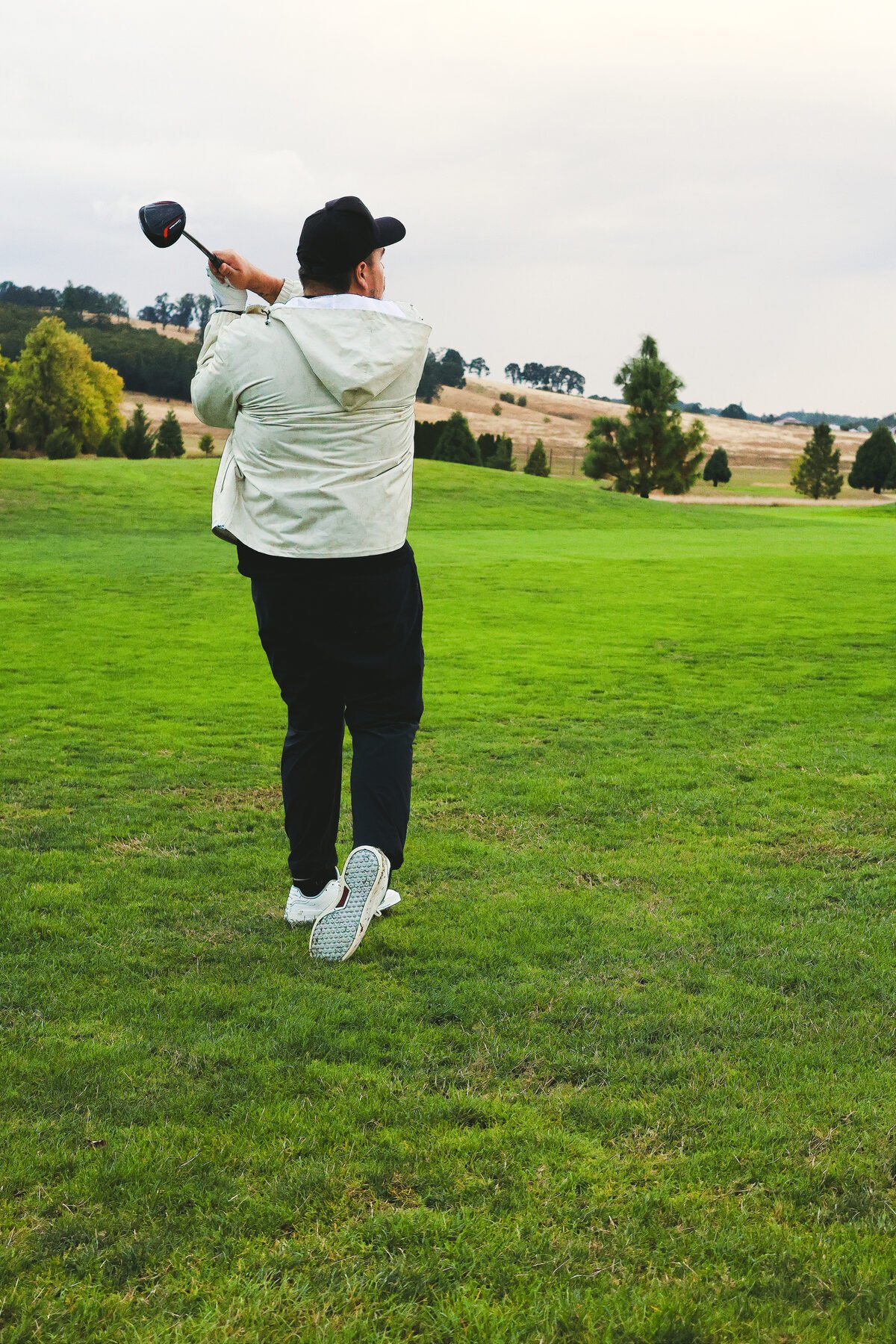 Finishing a drive, fairway dropping toward the treeline